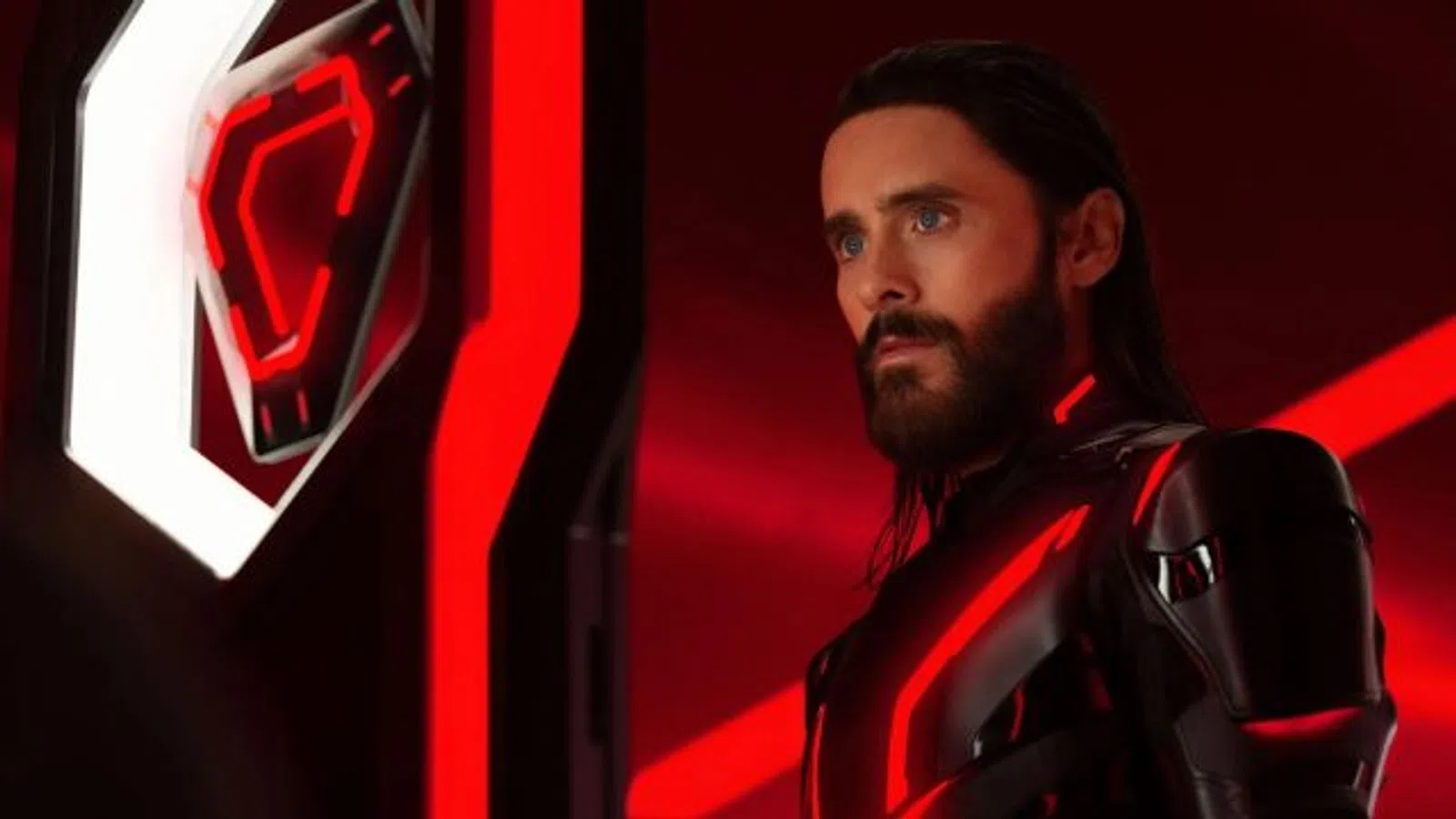 Man with beard in futuristic black suit with glowing red lights against red and black sci-fi background.