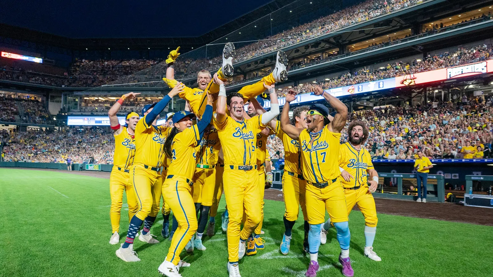 Baseball team in yellow uniforms celebrating on field with fans cheering in stadium at night game