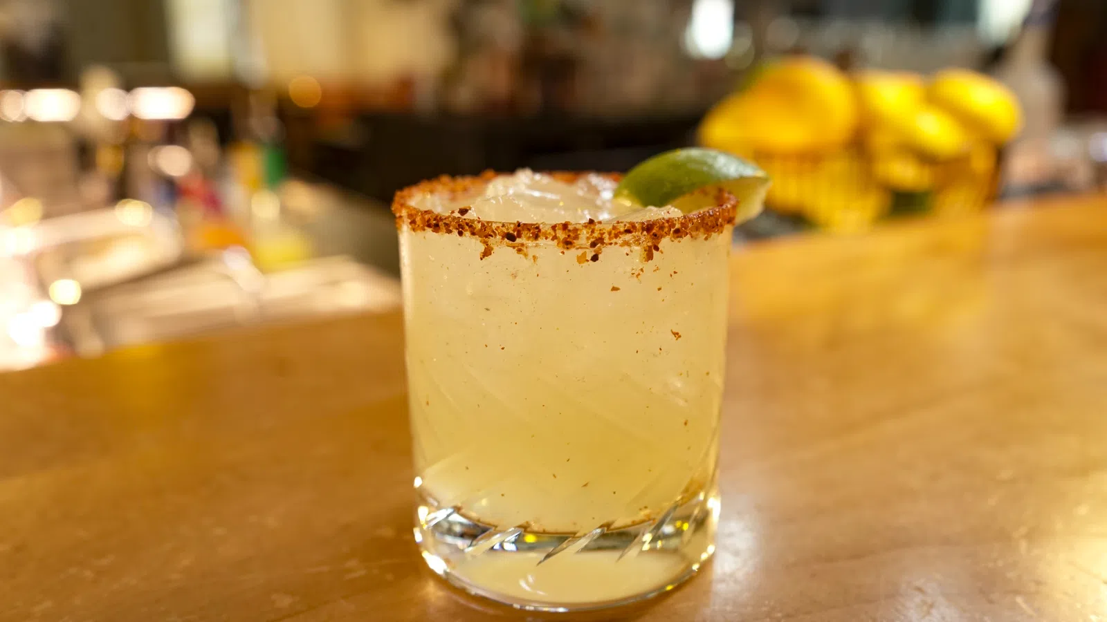 Chilled margarita cocktail with salted rim and lime wedge on wooden bar counter.
