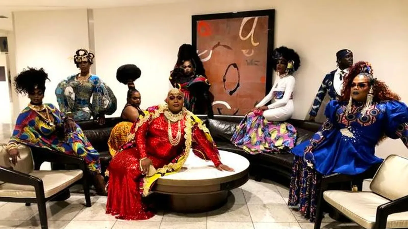 Group of people in colorful, traditional African-inspired attire posing in a modern lounge area around a round table.