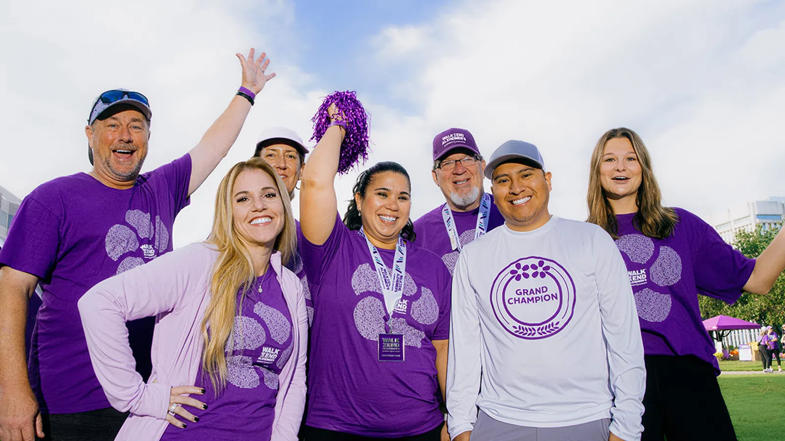 Group of diverse happy people wearing purple event shirts celebrating outdoors with a pom-pom and medals