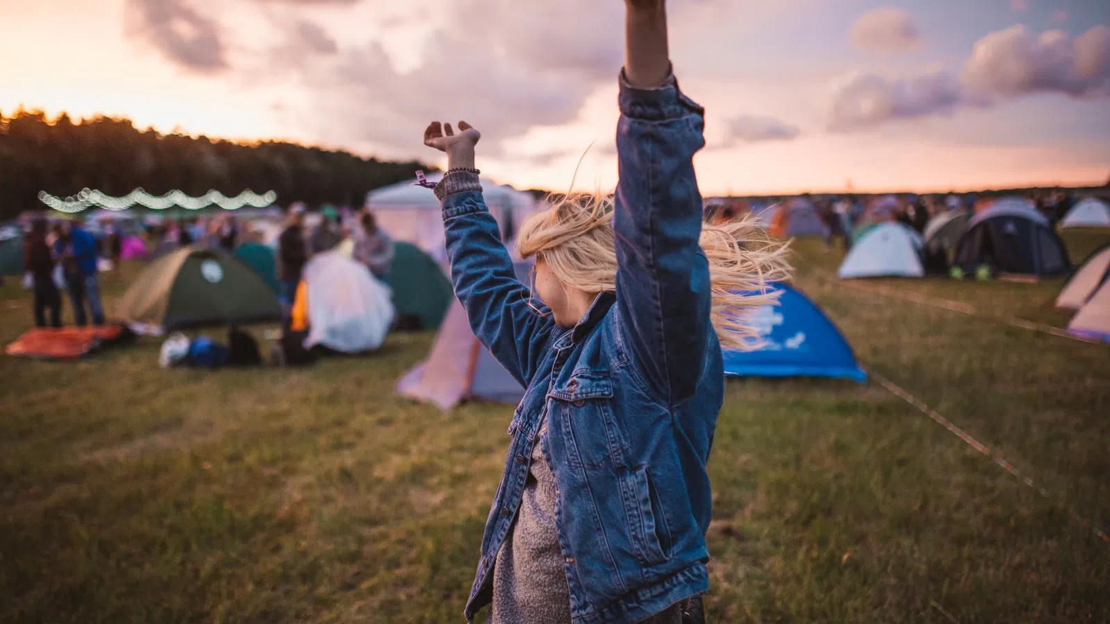 a person with the arms up in the air in front of a group of tents