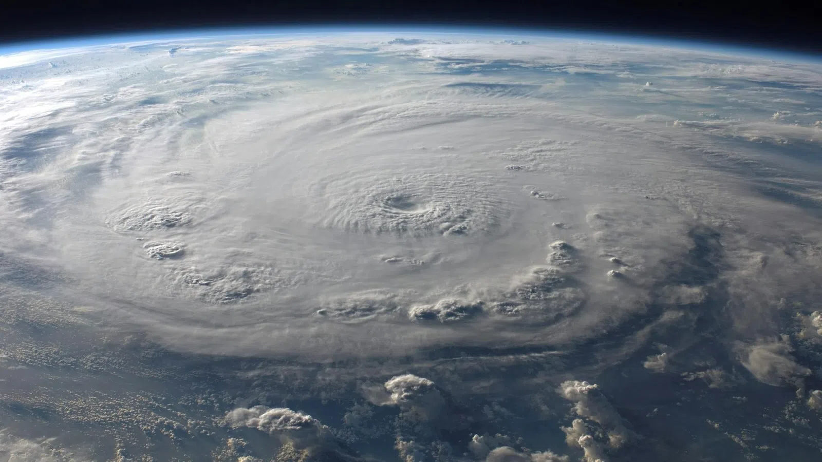 Satellite view of a massive hurricane with swirling cloud formations and a clear eye over the ocean.