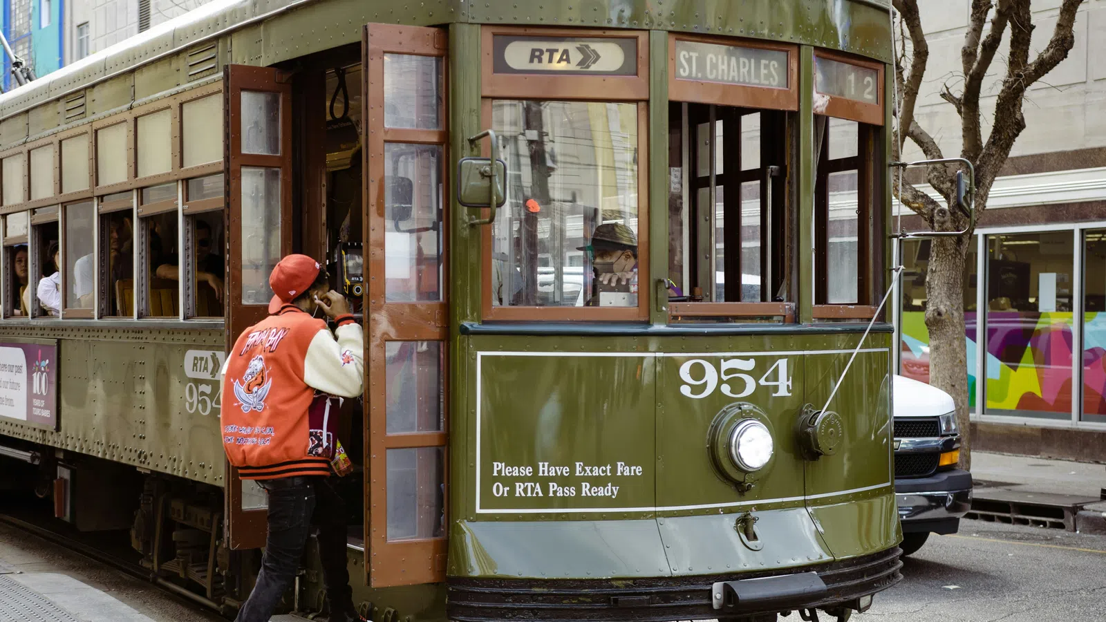 Green St. Charles streetcar number 954 in New Orleans boarding a passenger wearing a red jacket and cap