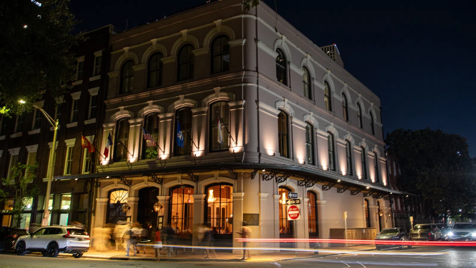 Historic corner building with arched windows illuminated at night with passing car light trails.