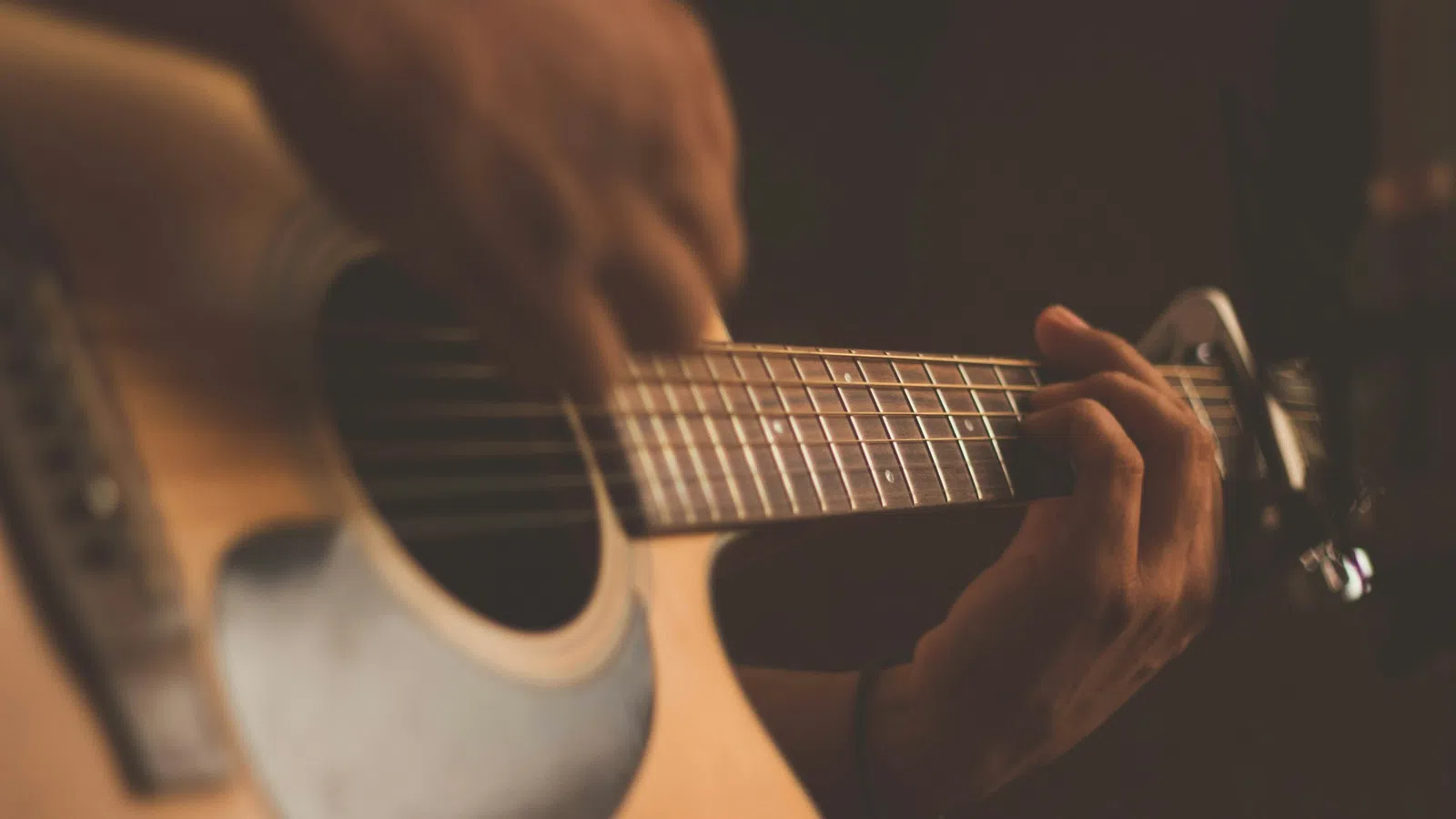 Close-up of hands playing an acoustic guitar with warm lighting and shallow depth of field.