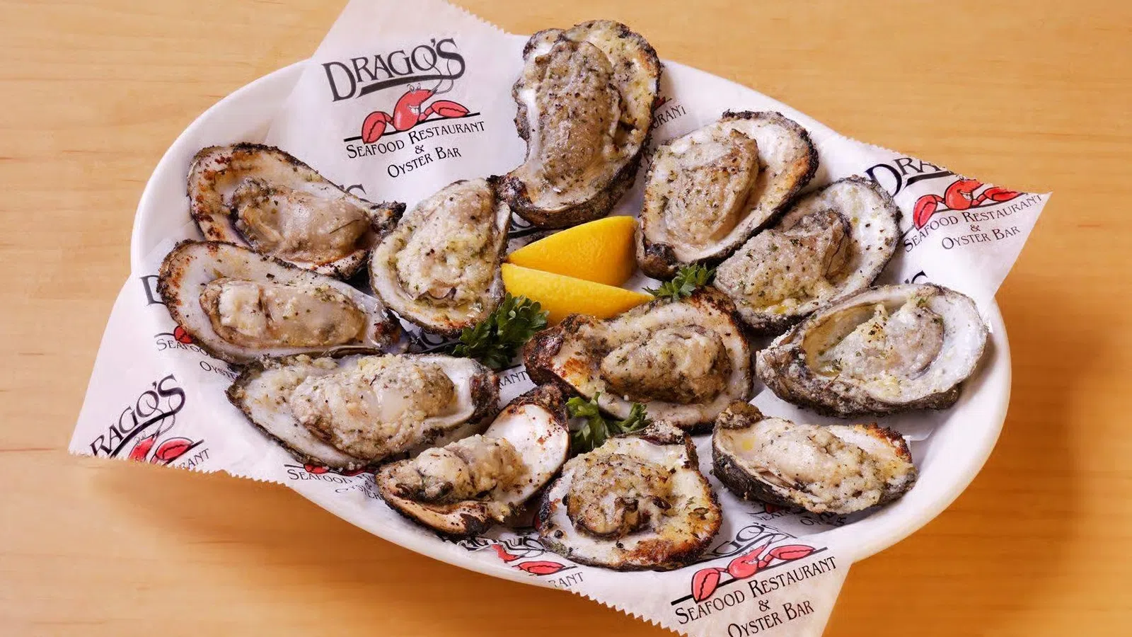 Plate of grilled oysters garnished with lemon wedges and parsley on branded seafood restaurant paper.