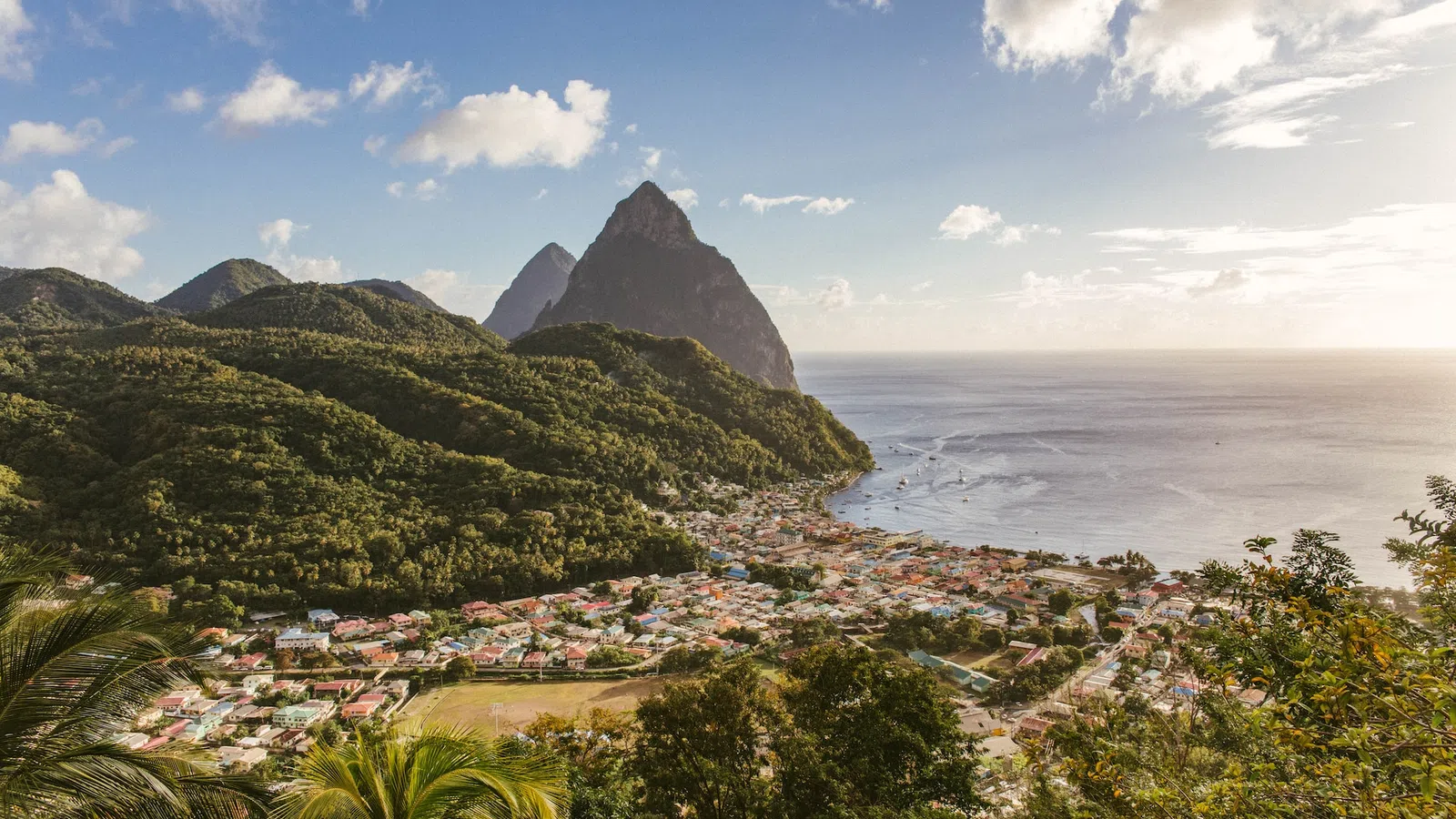 a beach with a town and mountains with Pitons in the background