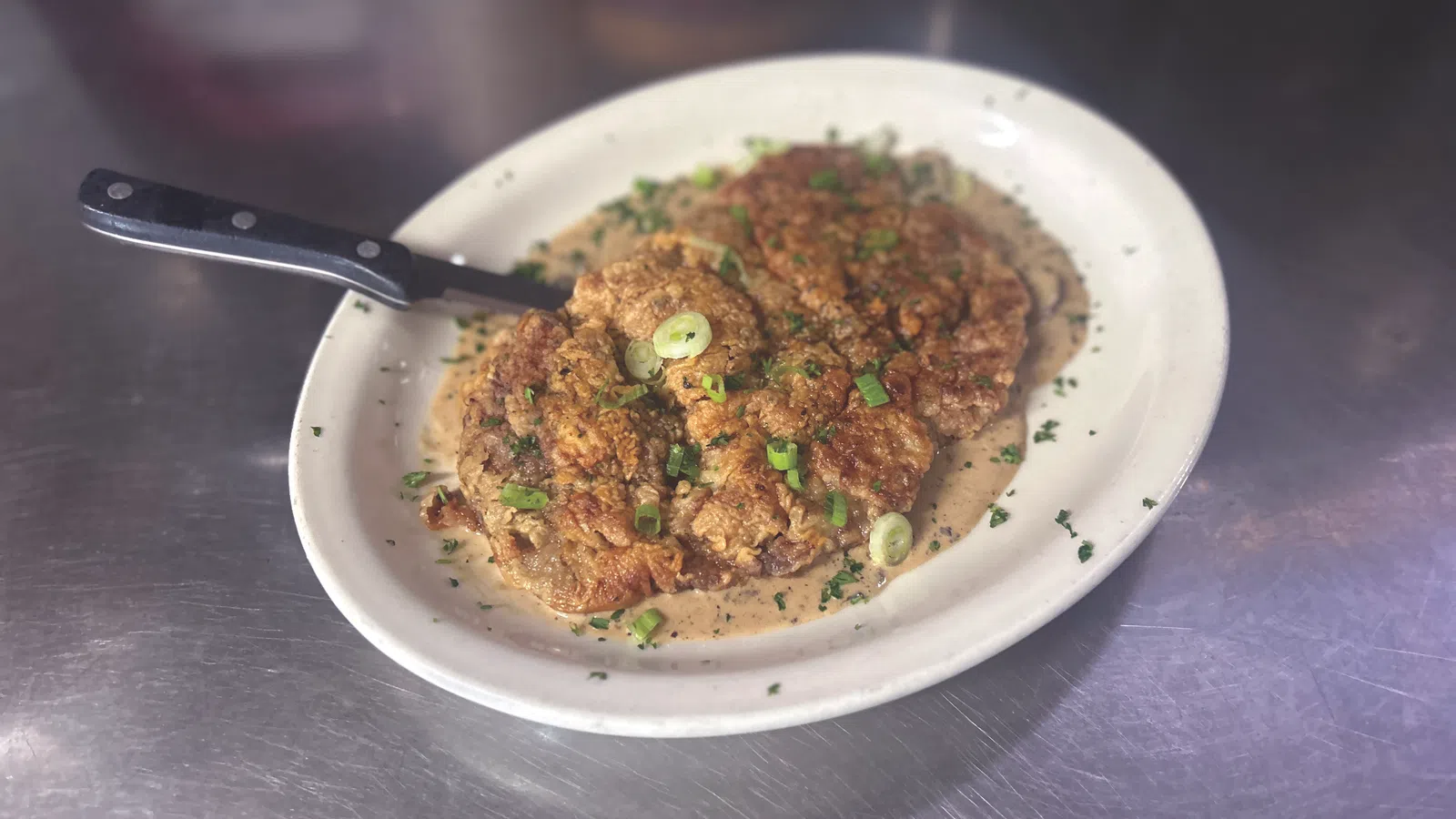 Plate with crispy fried chicken steak covered in creamy gravy and garnished with chopped green onions