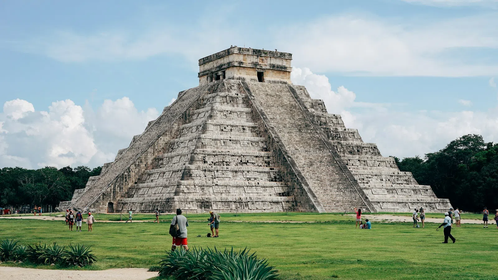 a pyramid with people walking around with Chichen Itza in the background