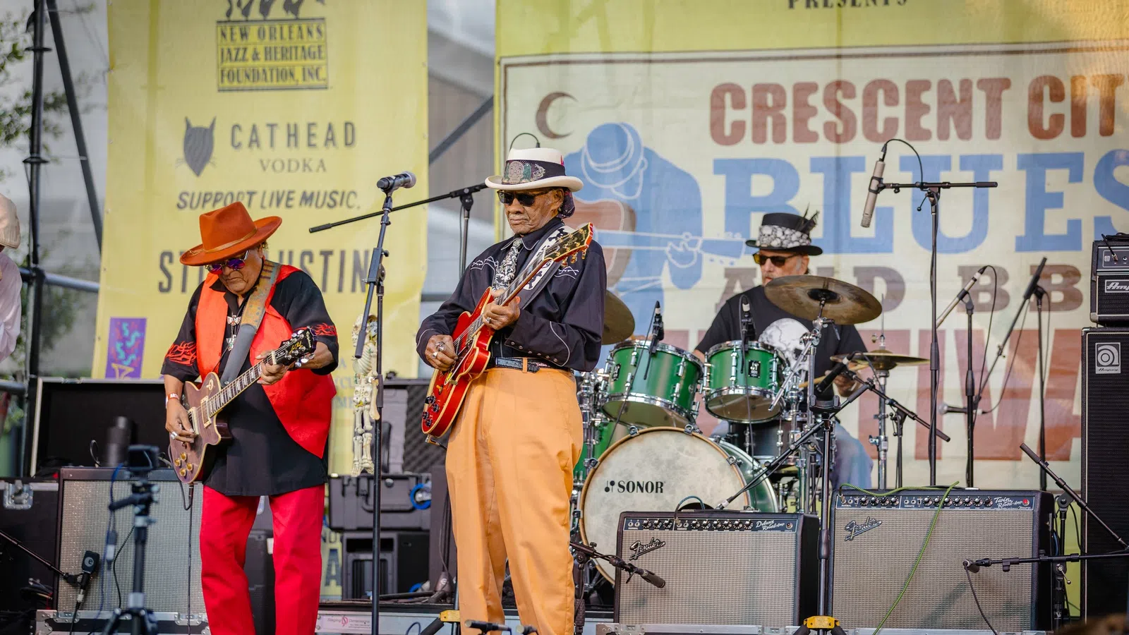 Three musicians performing live on stage at Crescent City Blues and BBQ Festival with guitars and drums.