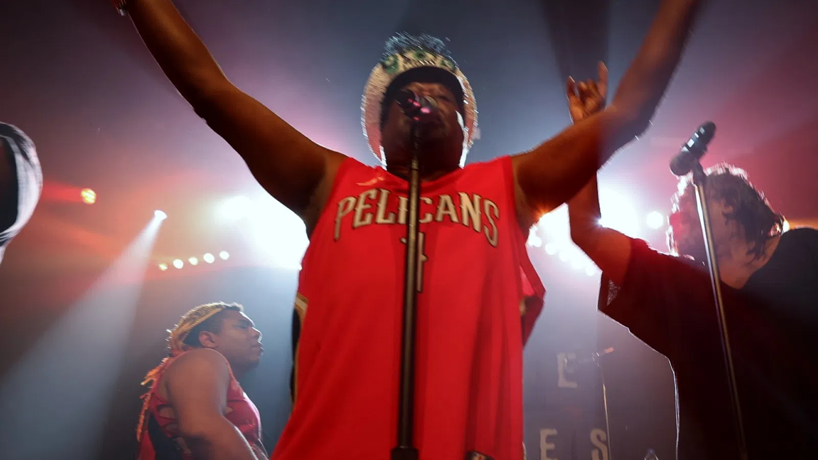 a man wearing a red shirt and holding his arms up in front of a microphone