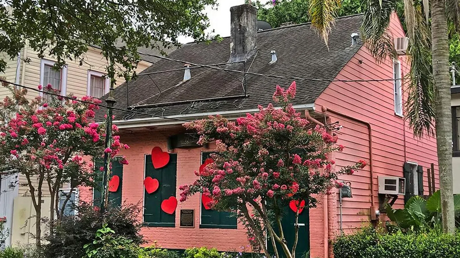 Pink house decorated with red hearts on windows and a rainbow pride flag flying on the rooftop.
