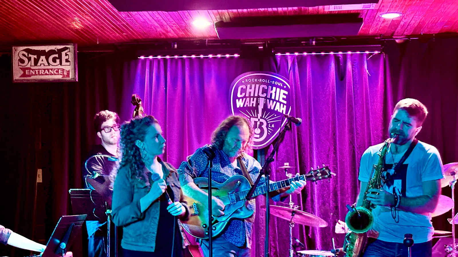 Live band performing with guitar, saxophone, vocals, and keyboard on stage at Chickie Wah Wah venue.
