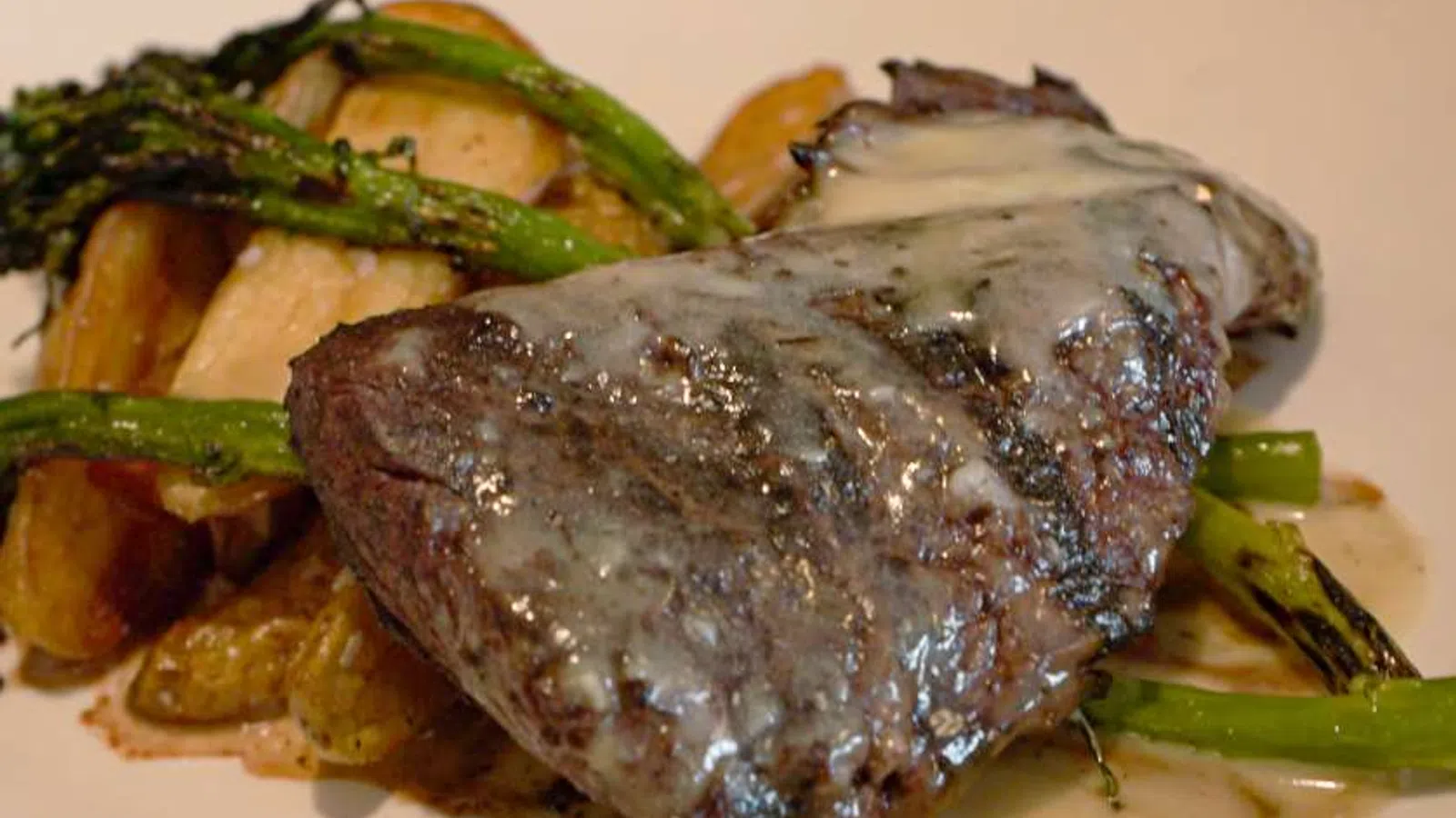 Grilled steak with creamy sauce served with roasted potatoes and asparagus on a white plate.