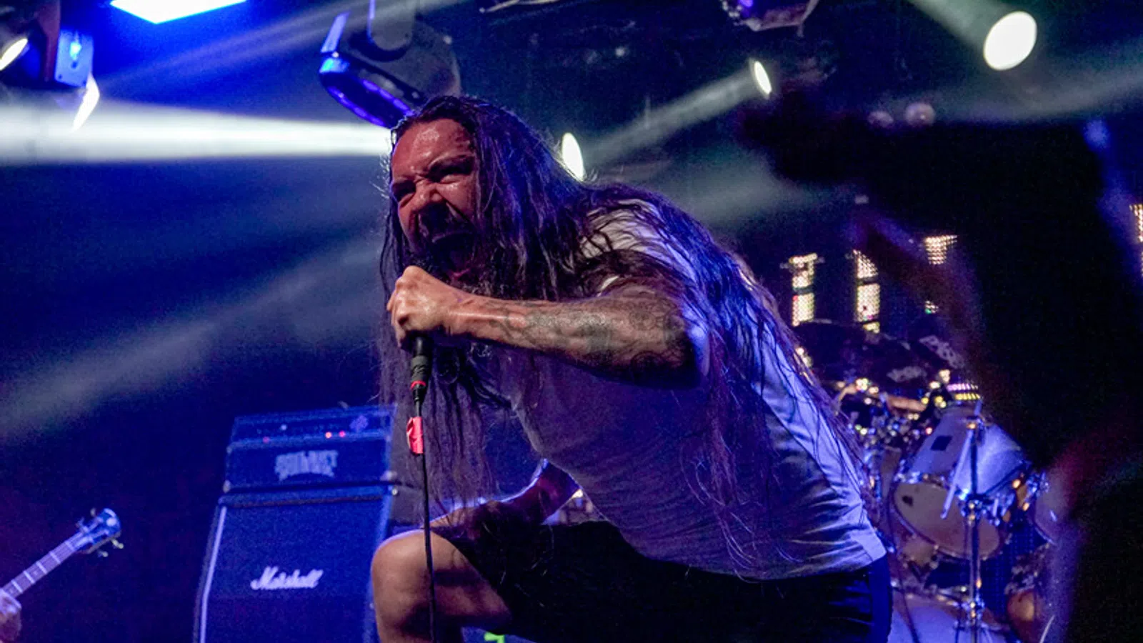 a man with long hair holding a microphone in front of a drum set