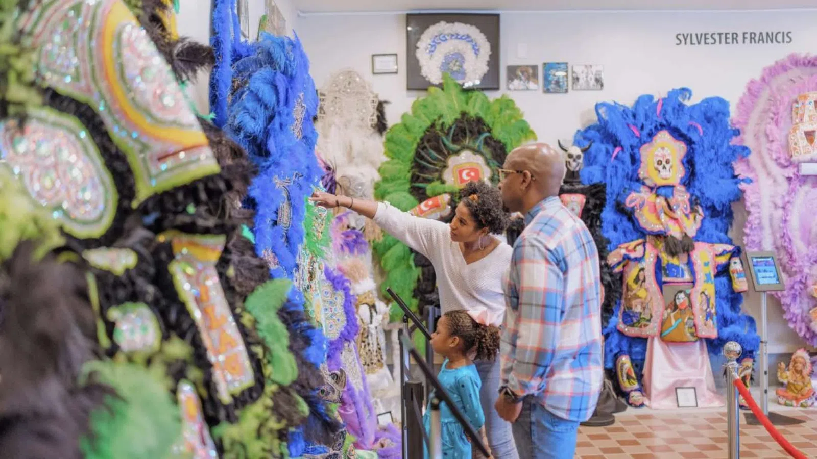 Family explores colorful, feathered Mardi Gras Indian costumes in an indoor cultural exhibit.