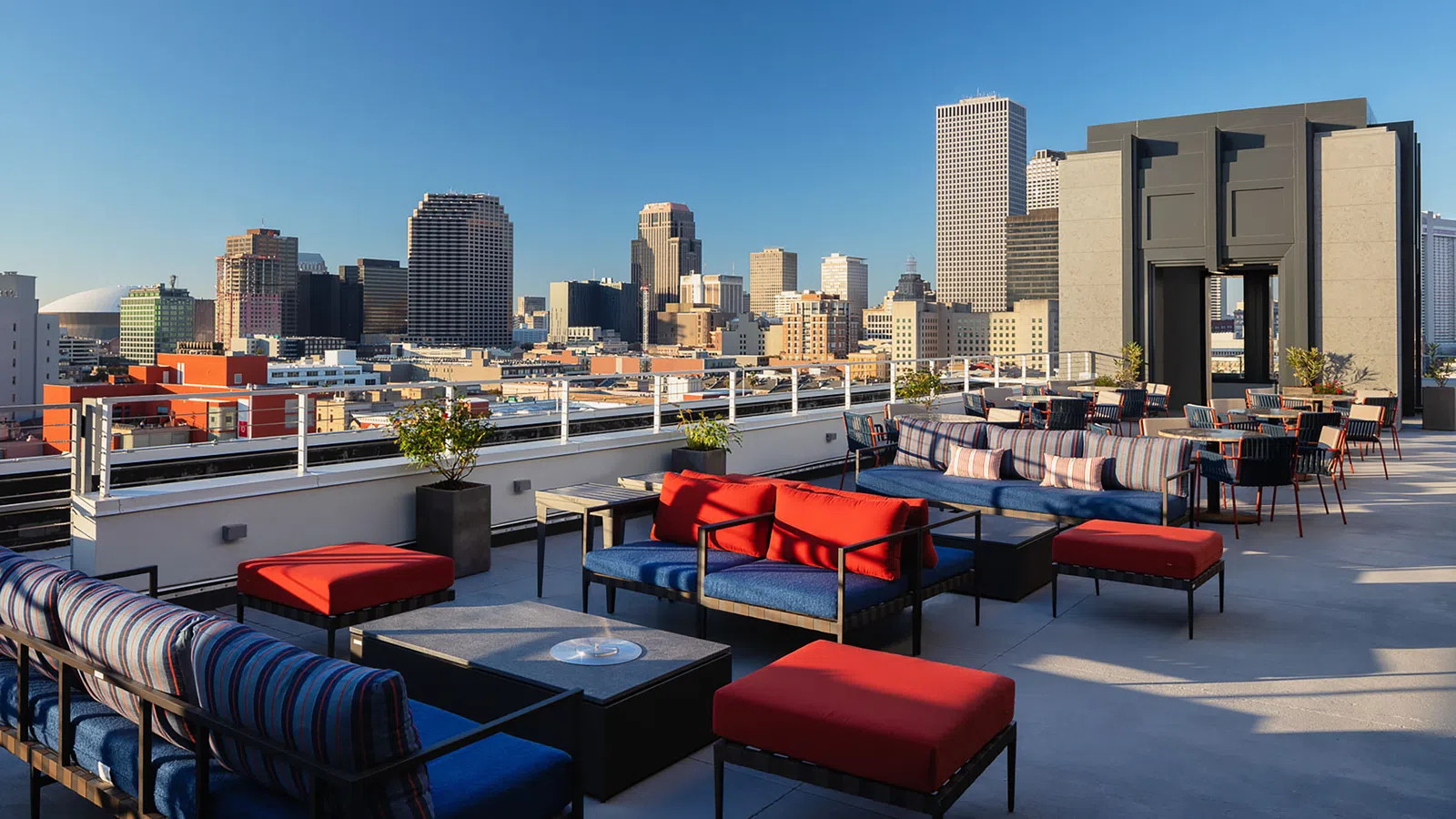 Stylish rooftop lounge with city skyline view and modern furnishings under a clear blue sky.
