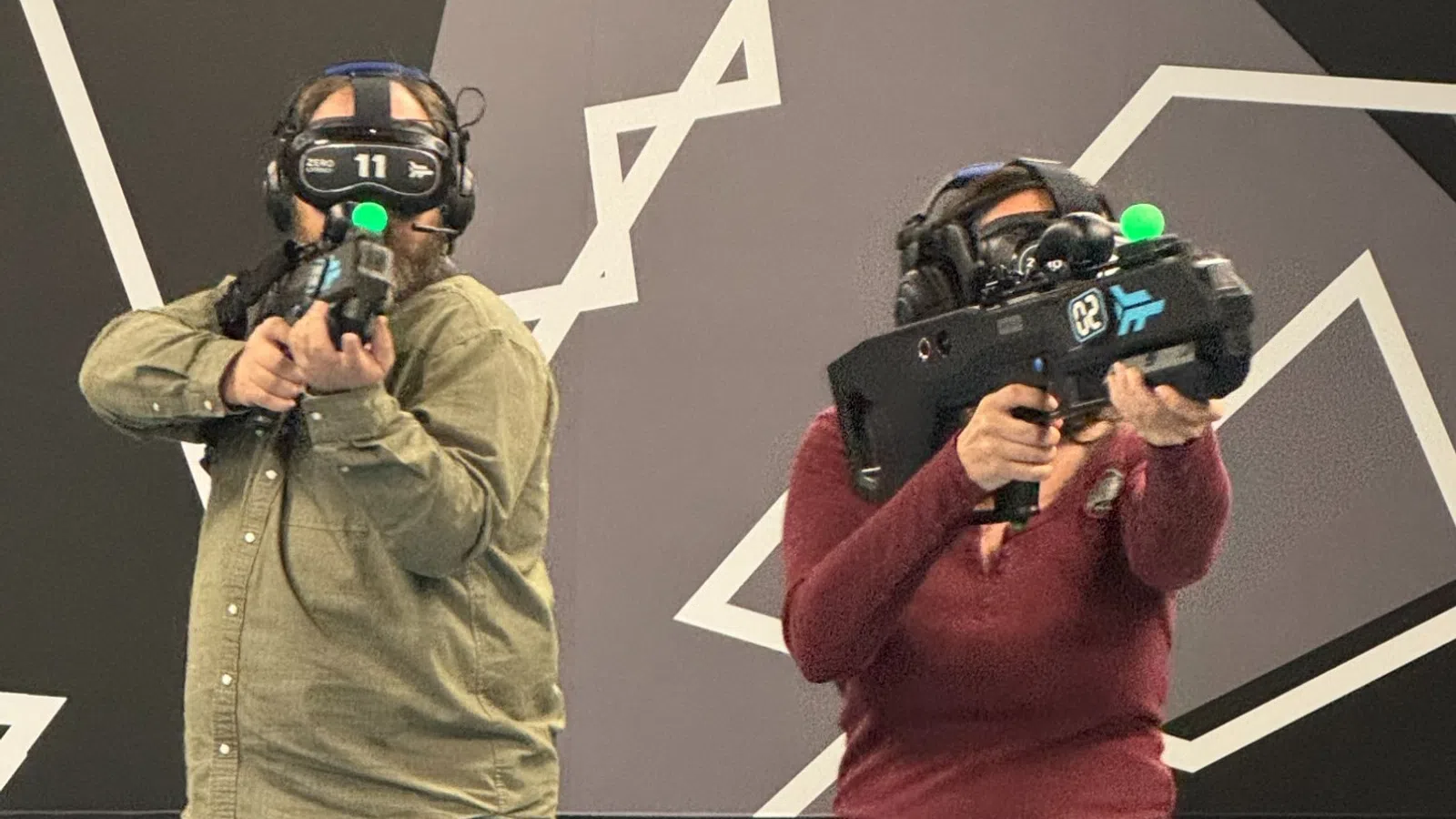 Two people wearing VR headsets and holding controllers in a modern room with geometric wall and floor designs.