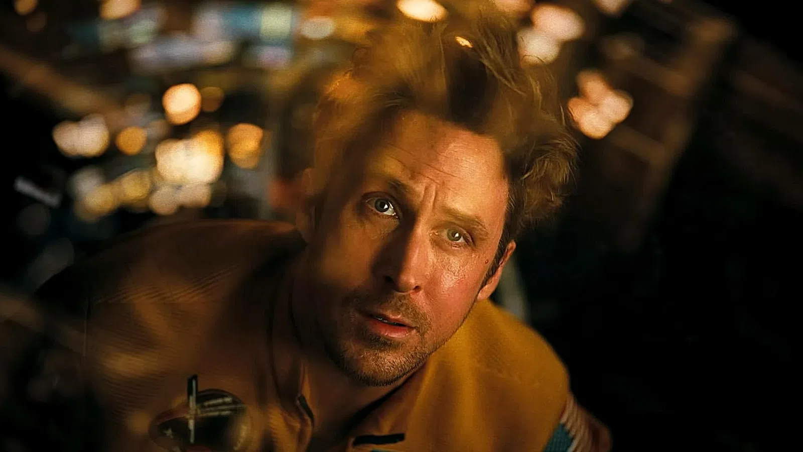 Man with intense expression looking upward in a dimly lit room with blurred lights in the background