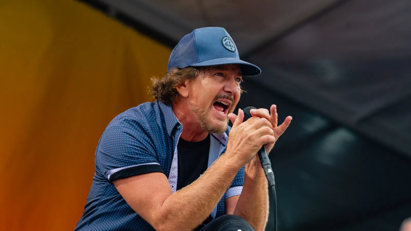 Male singer passionately performing on stage wearing a blue cap and shirt, holding a microphone.