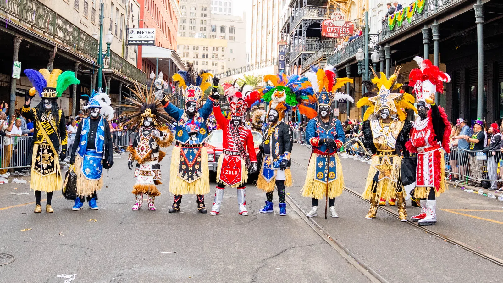 Colorful Mardi Gras Zulu tribe members in ornate costumes and feathered headdresses standing in a New Orleans street parade.