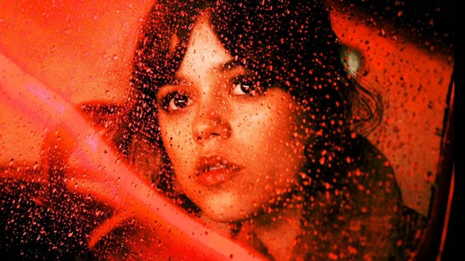 Young woman looking through a rain-streaked window with warm red ambient lighting