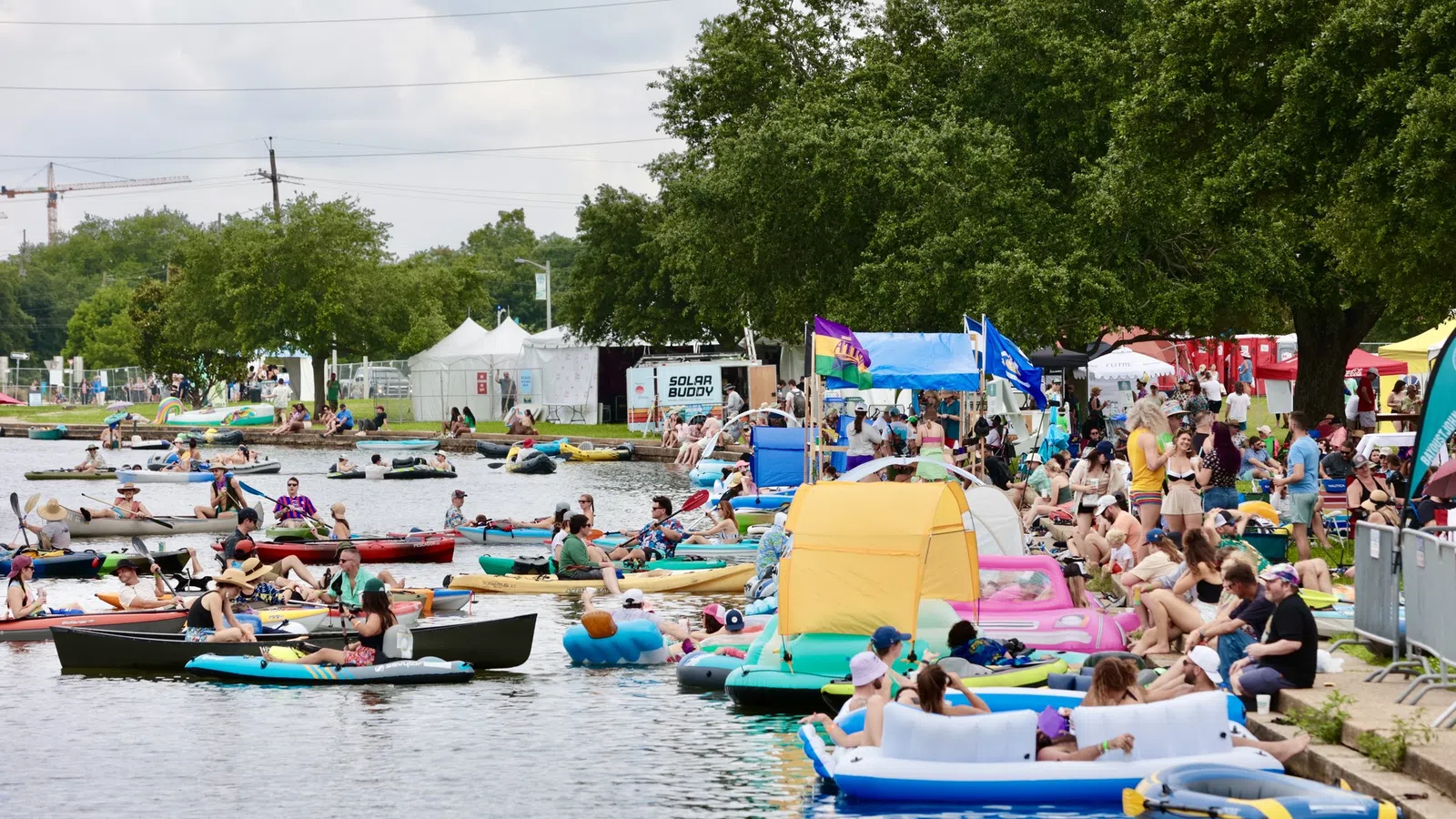 Crowd enjoying a summer festival by the water with kayaks and colorful inflatables.