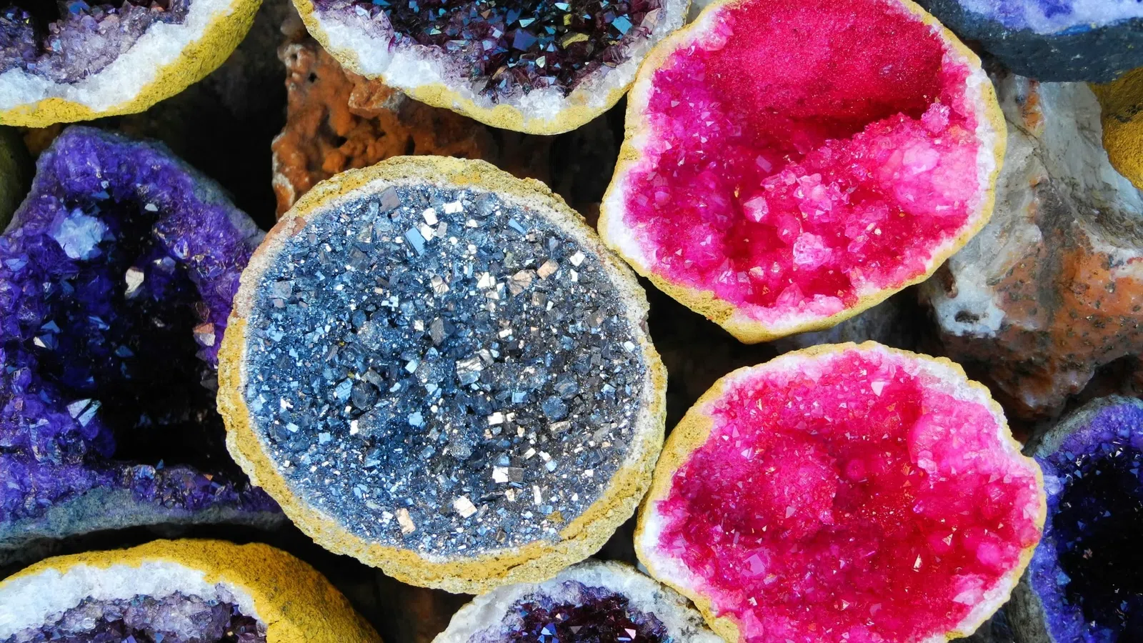 Close-up of colorful geode crystals in shades of purple, blue, pink, and black with rough outer shells.