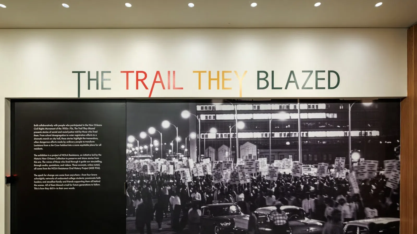 Black and white photo of a civil rights march under The Trail They Blazed exhibition title on a museum wall.