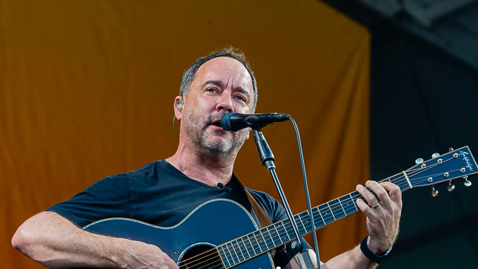 Musician performing on stage, playing an acoustic guitar with a microphone.