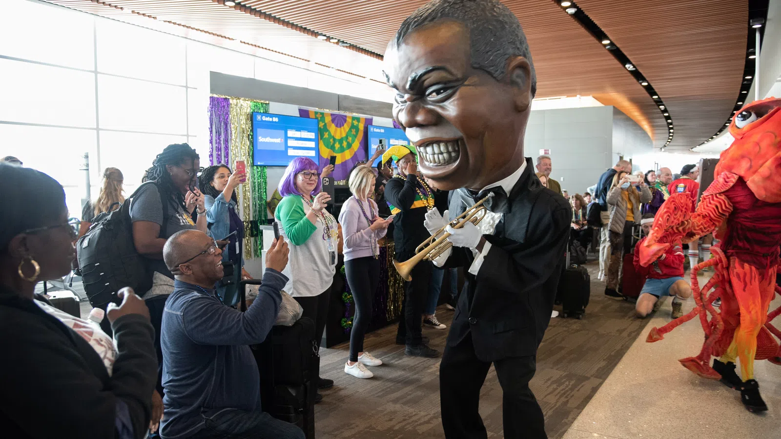 Crowd at indoor event watches performer in big mask playing trumpet and another performer in lobster costume.