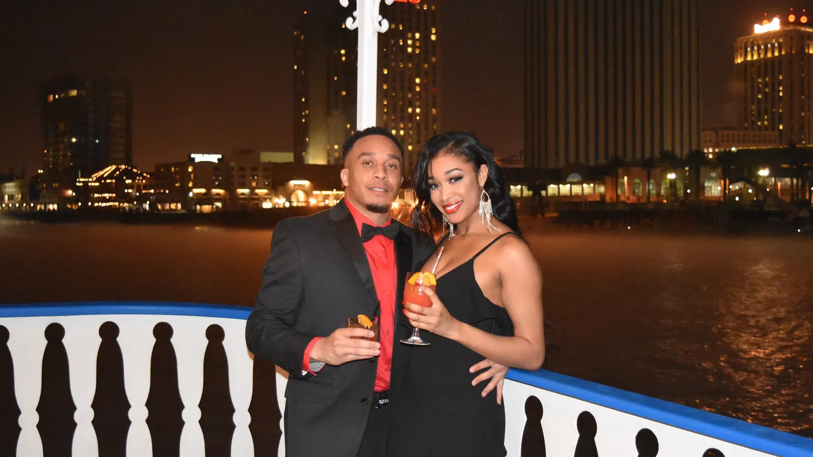 a man and woman posing for a picture with a body of water in the background