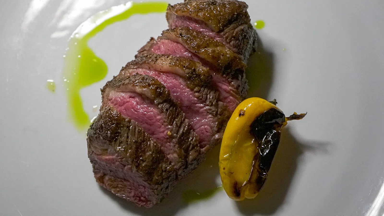a piece of meat with a green and yellow substance on a white plate