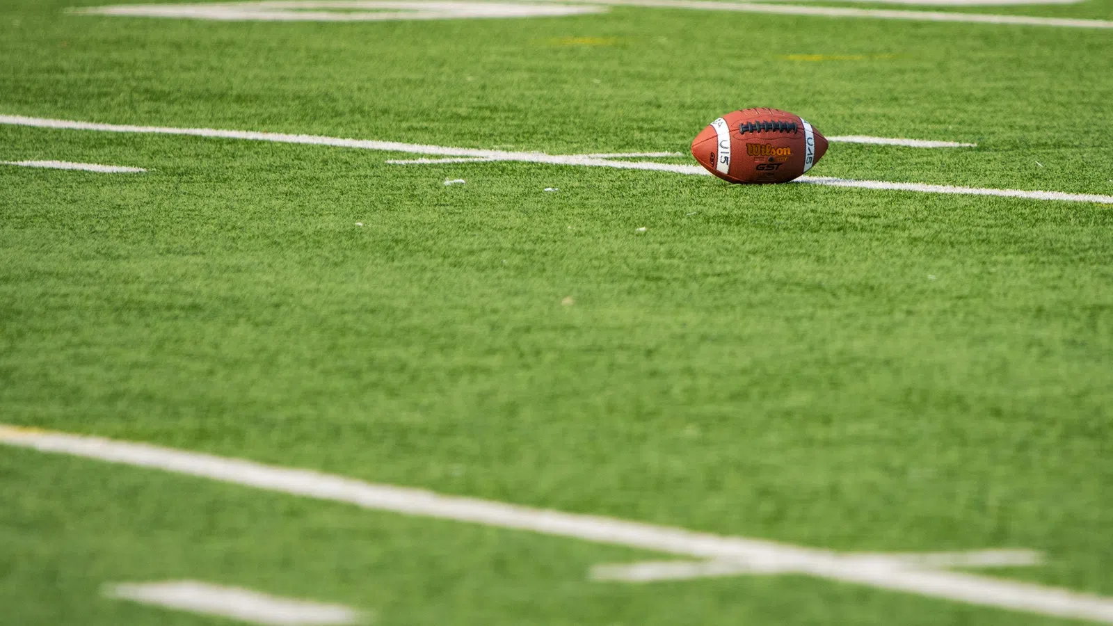 American football resting on green turf near white yard lines on a sunny day at the stadium