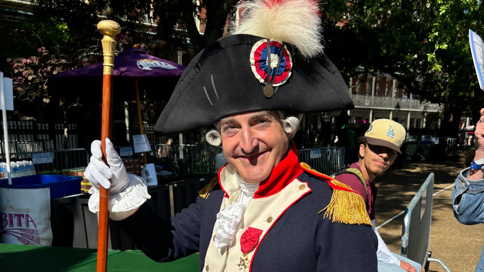 Man in historical costume smiling, dressed as a revolutionary figure with a tall hat and staff.