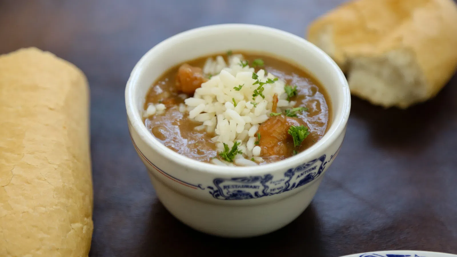 Bowl of gumbo topped with rice and parsley, served with bread on a dark surface.
