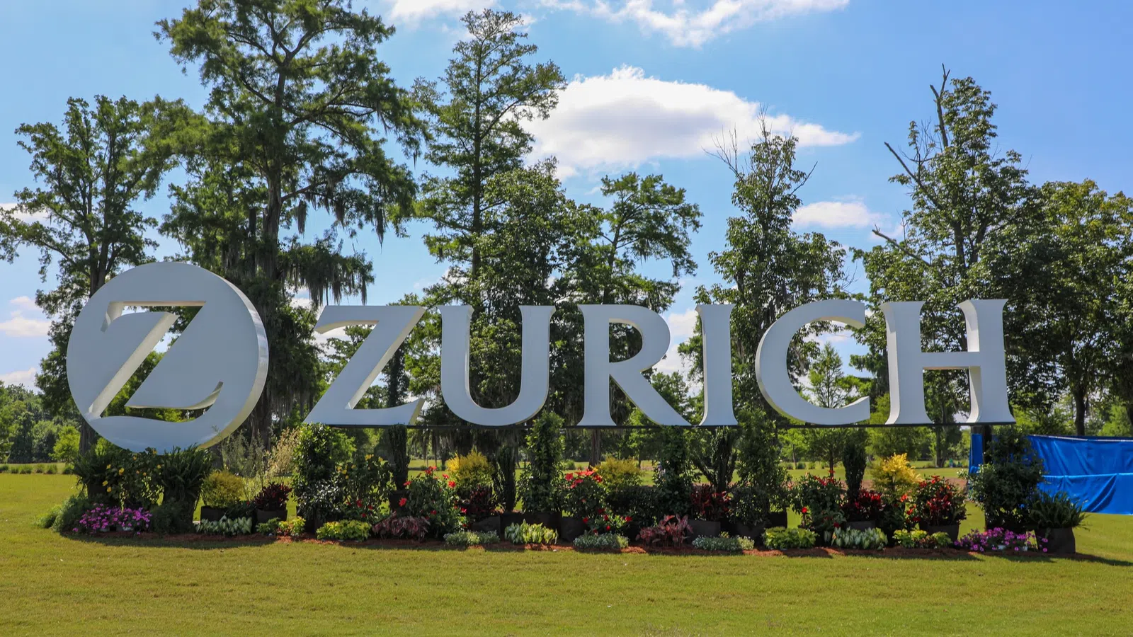Zurich company sign in a landscaped setting with trees and flowers under a blue sky.