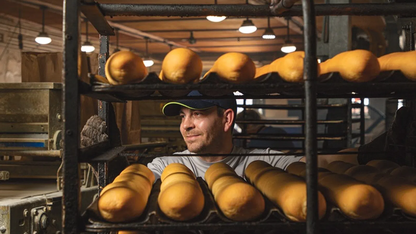 a person in a hat behind a shelf of breads