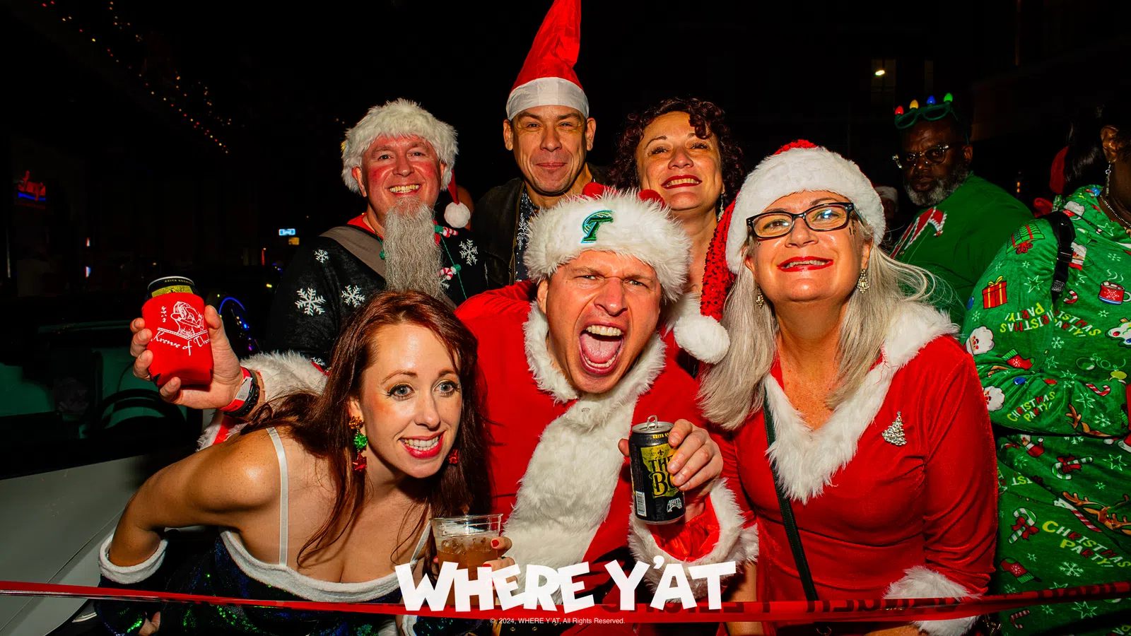a group of people wearing santa hats and holding cans of beer