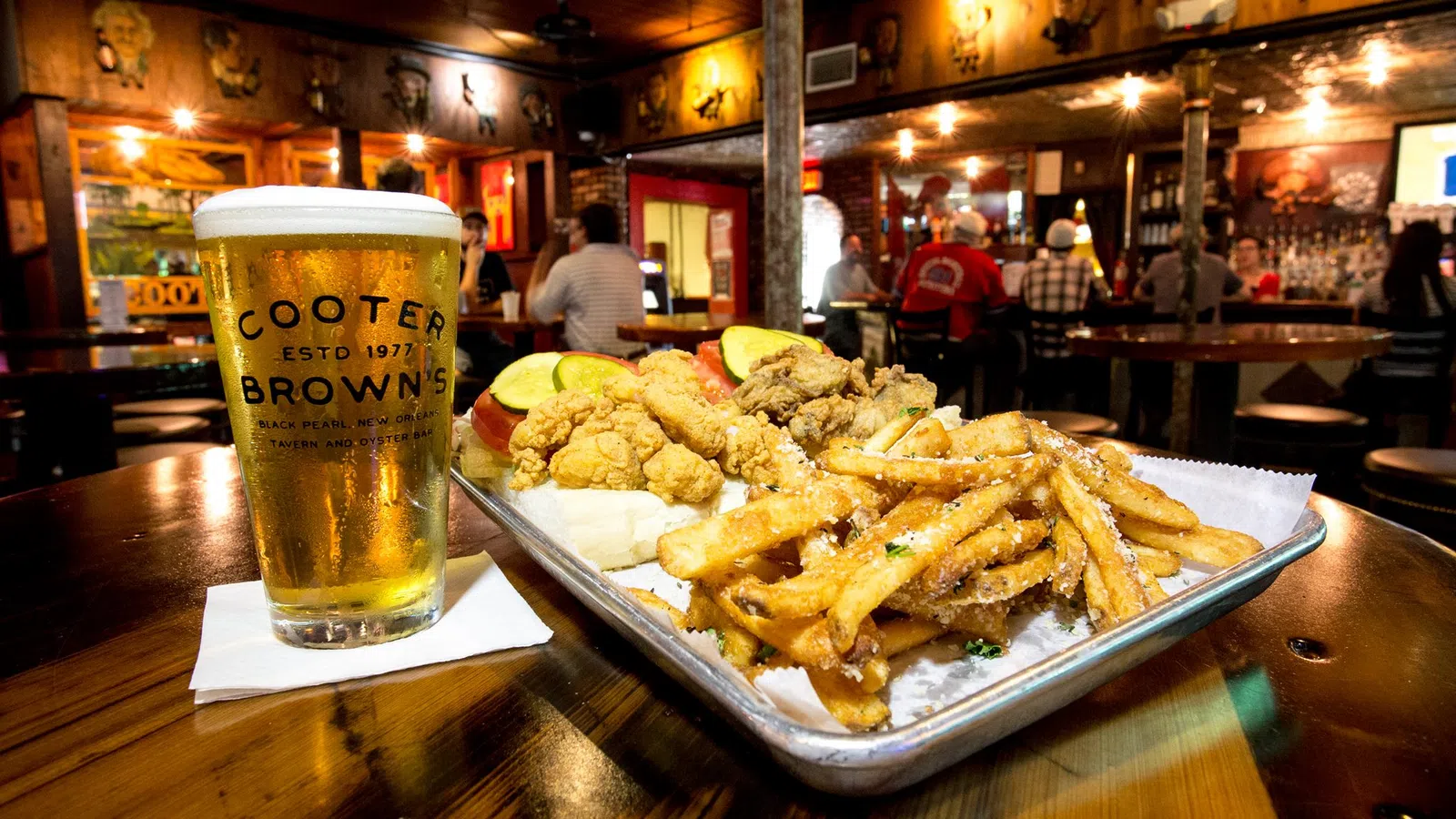Tray of fried seafood, fries, and pickles with a cold beer in a cozy bar setting at Cooter Brown's.