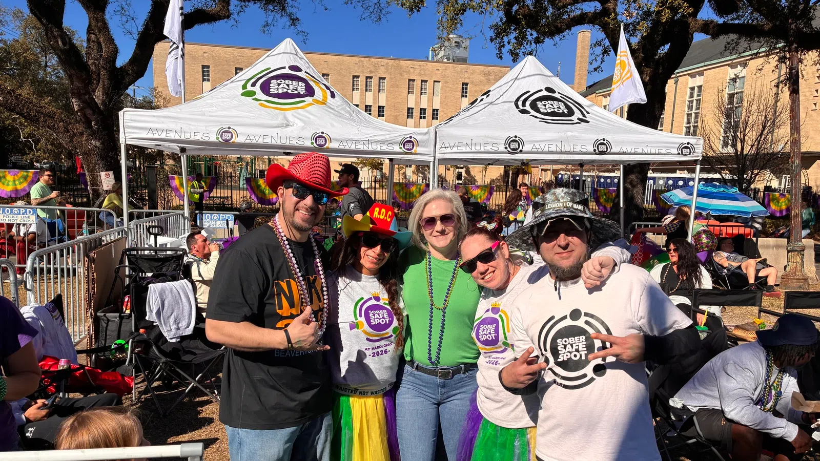 Group of five people wearing colorful tutus and Sober Safe Spot shirts at an outdoor event under tents