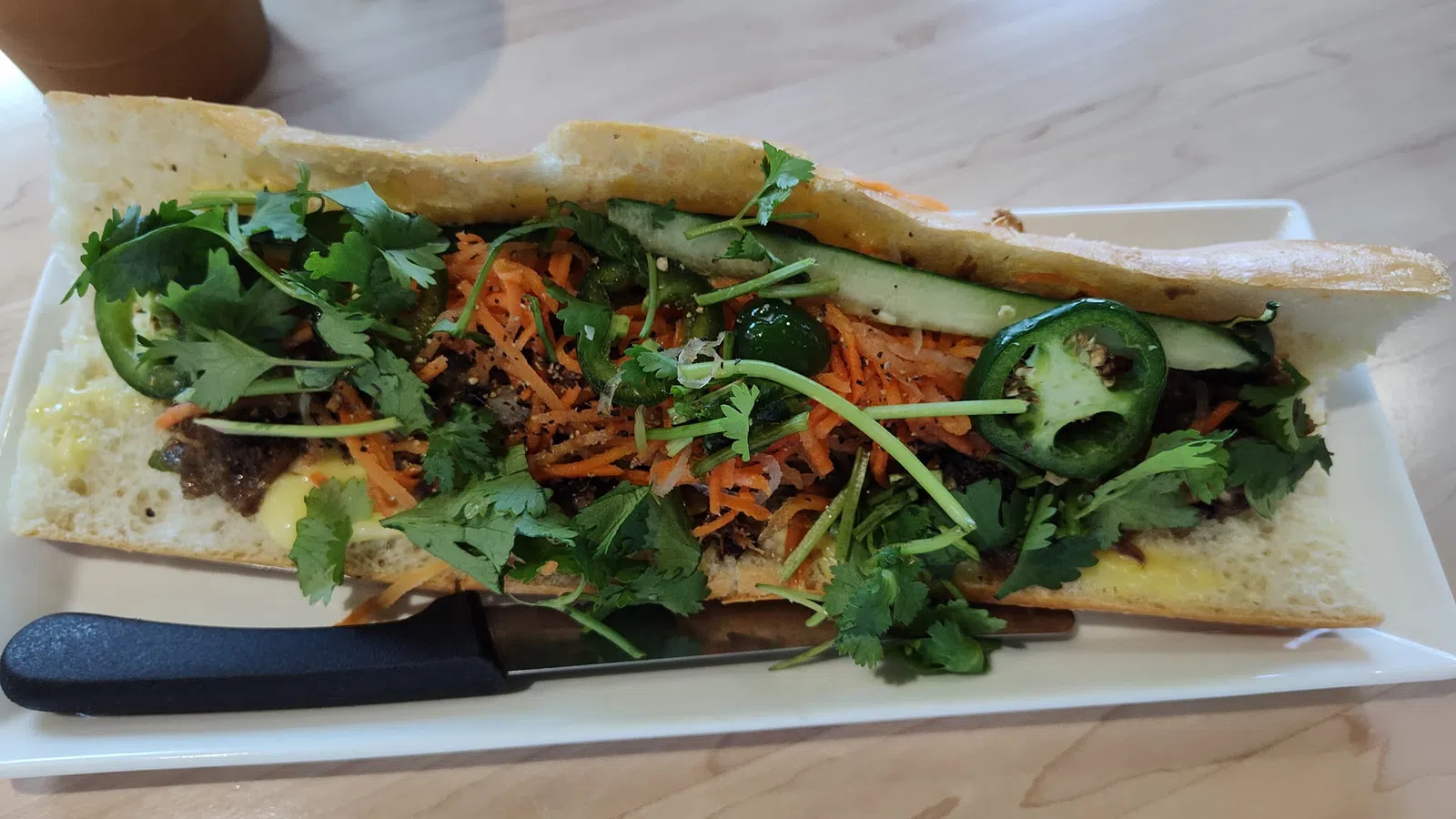 Vietnamese banh mi sandwich with cilantro, cucumber, jalapeno, shredded carrots, and bread on a white plate.