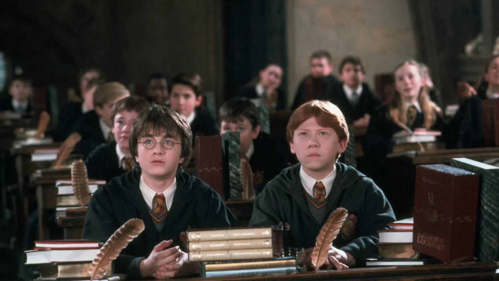 a couple of boys sitting at a table with books and Rupert Grint et al. in the background