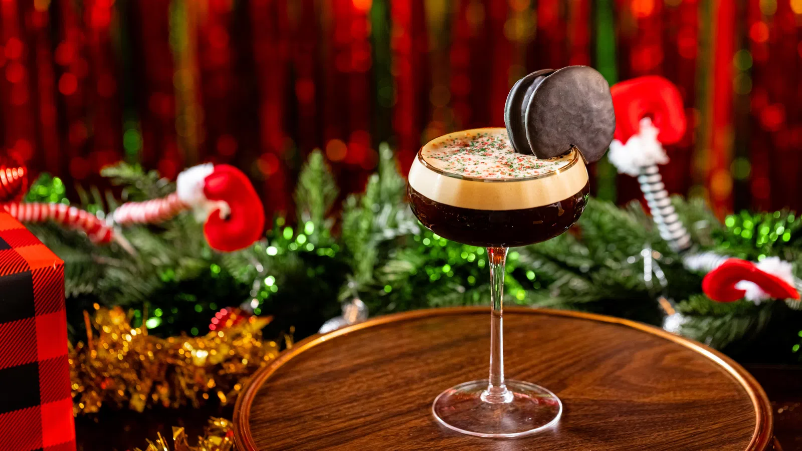 Festive holiday cocktail with creamy foam and chocolate garnish on wooden surface with Christmas decorations.