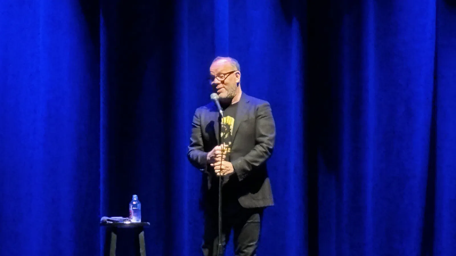 a man standing at a podium with a microphone and a blue curtain