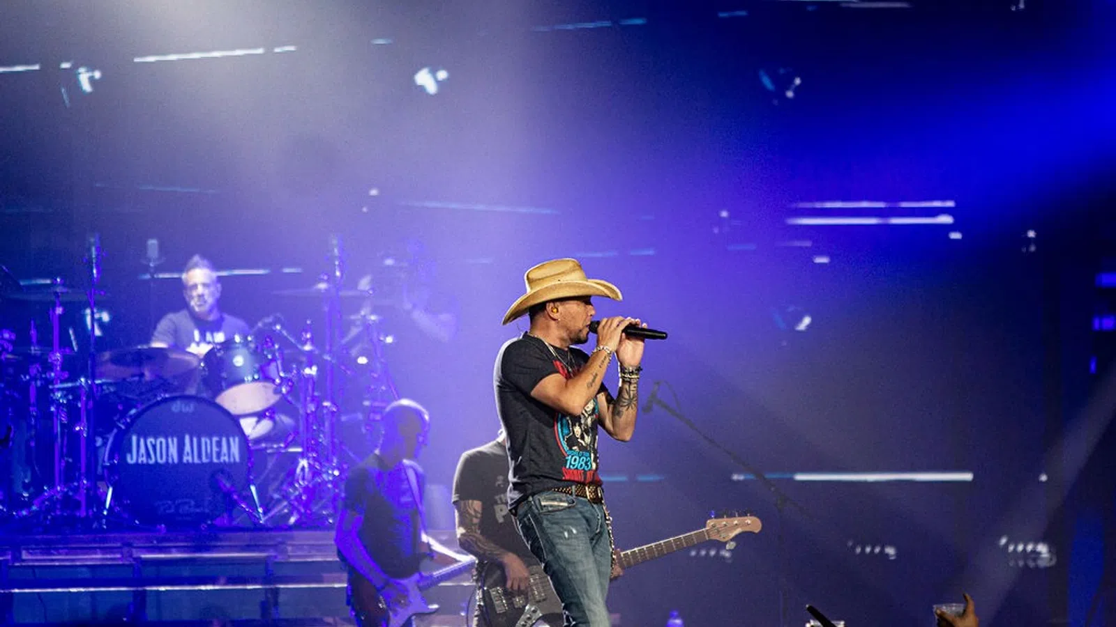 a man singing into a microphone on stage with a band playing