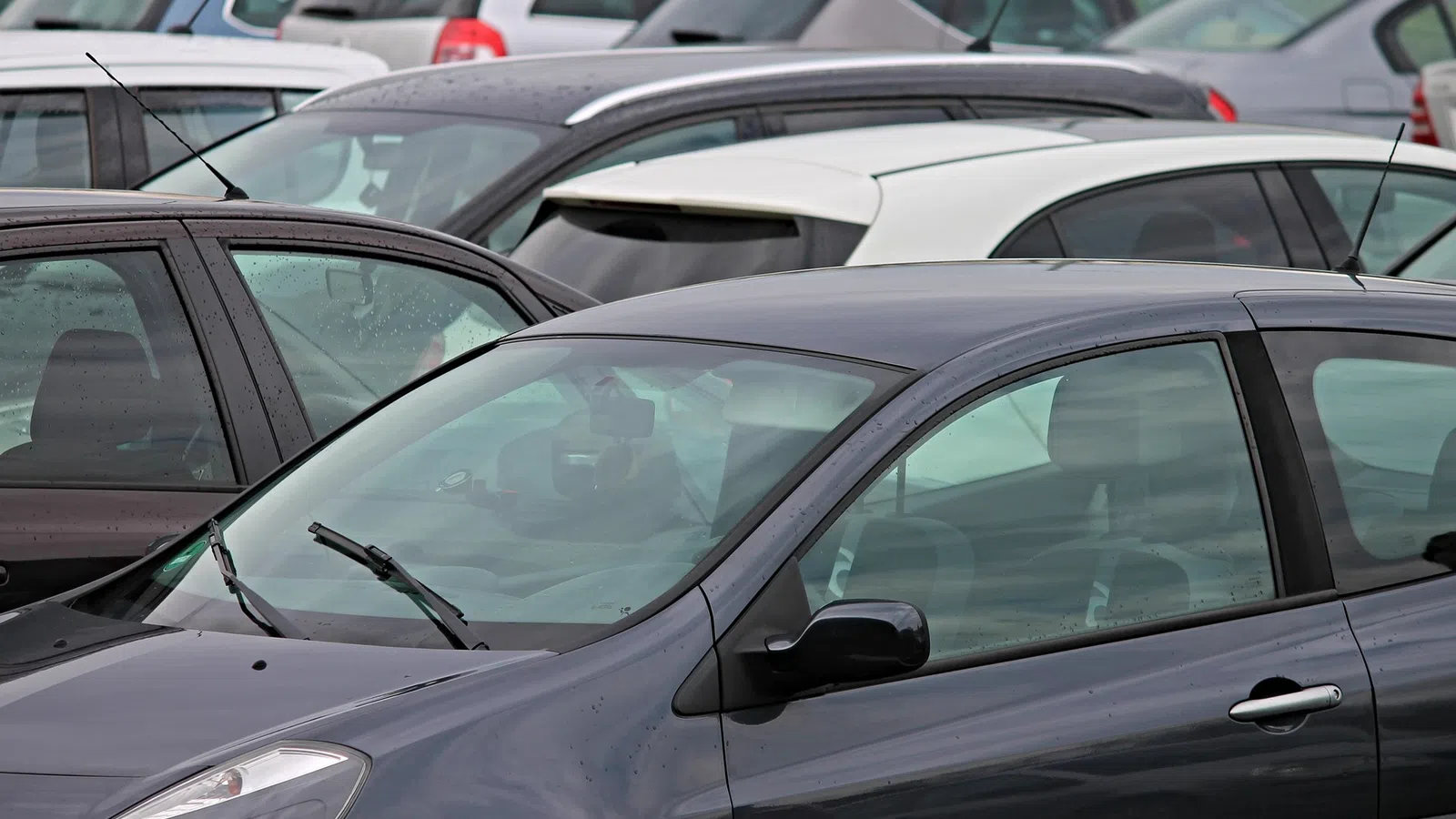Close-up of multiple parked cars in a crowded parking lot on a cloudy day with raindrops visible on windows.
