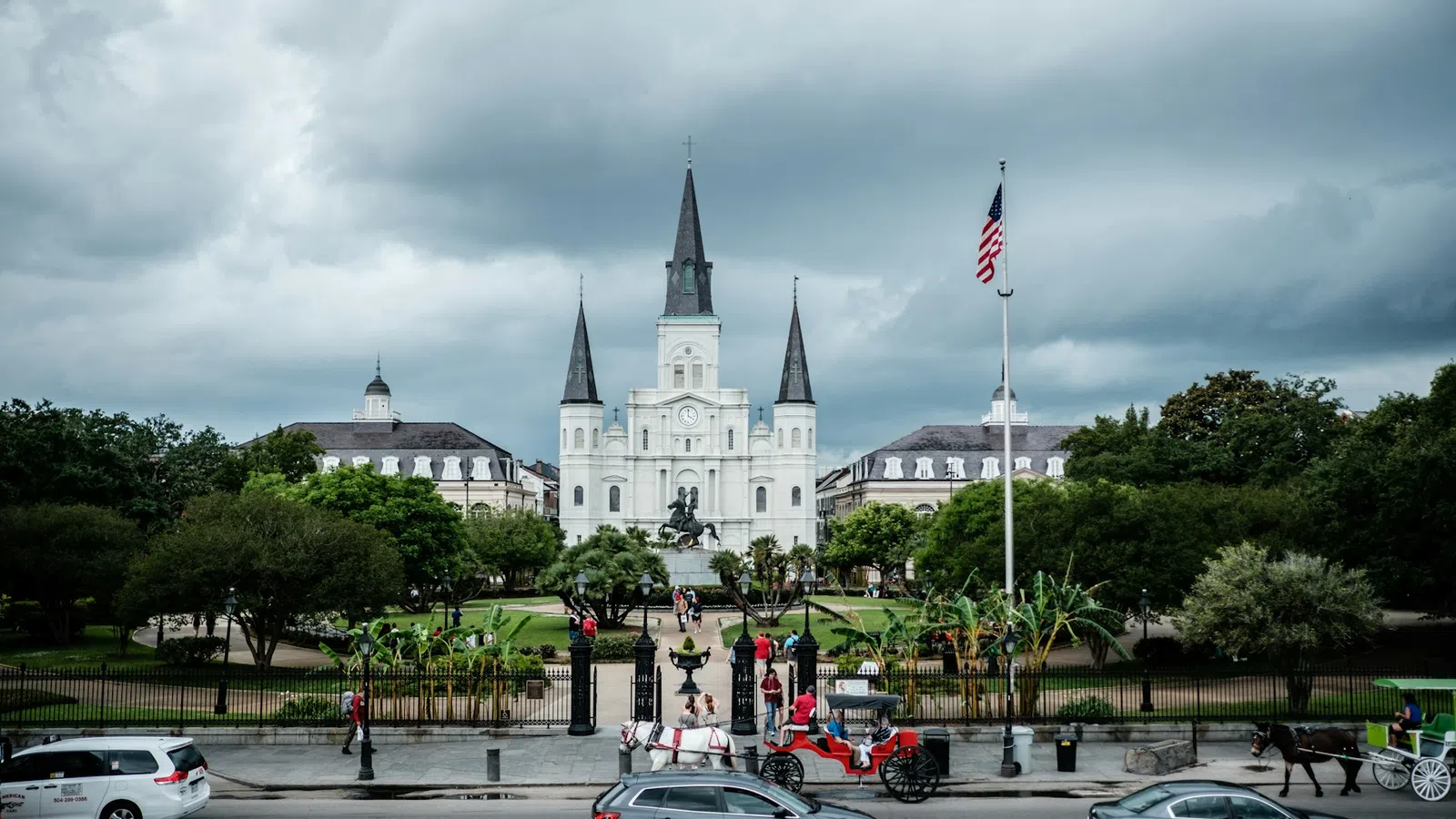 St. Louis Cathedral with horse-drawn carriages and cars on street under cloudy sky in New Orleans