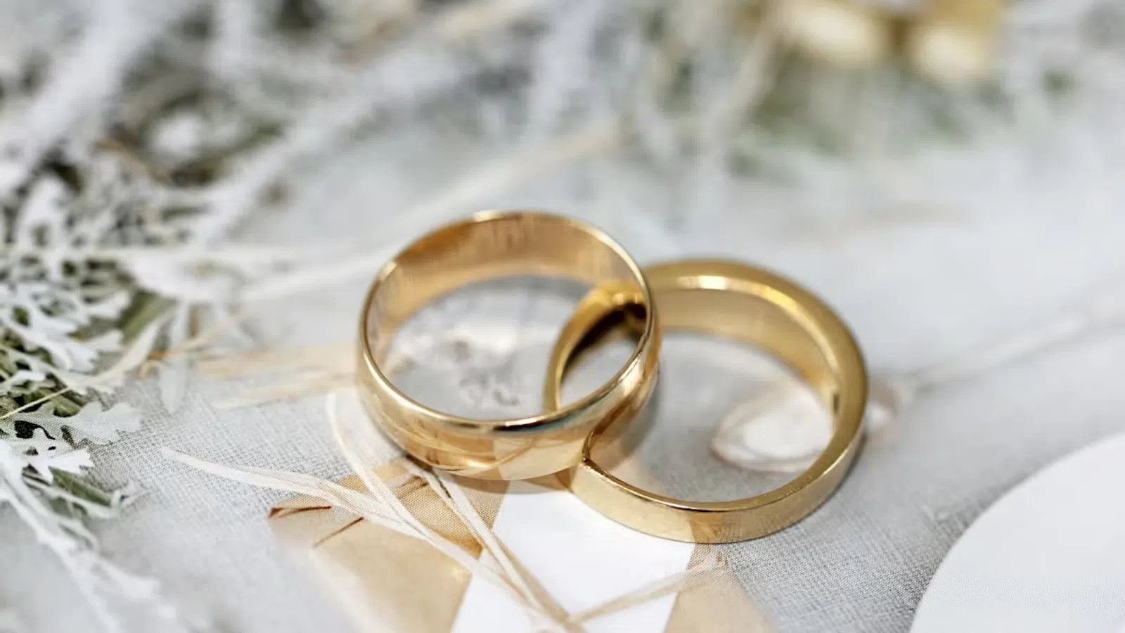 Two gold wedding rings resting on a soft fabric surface with delicate dried flowers in the background